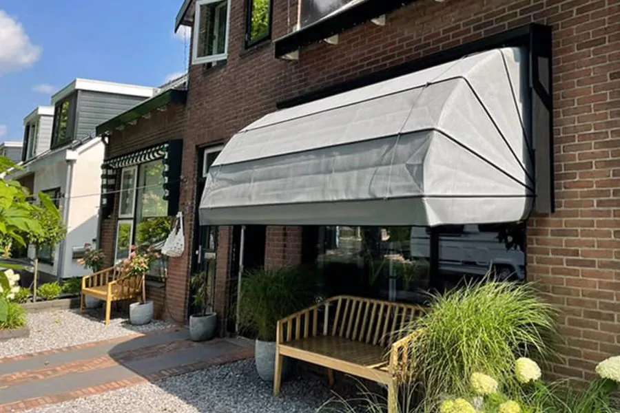 Moderne grijze markies met aluminium frame boven een groot raam aan een bakstenen gevel