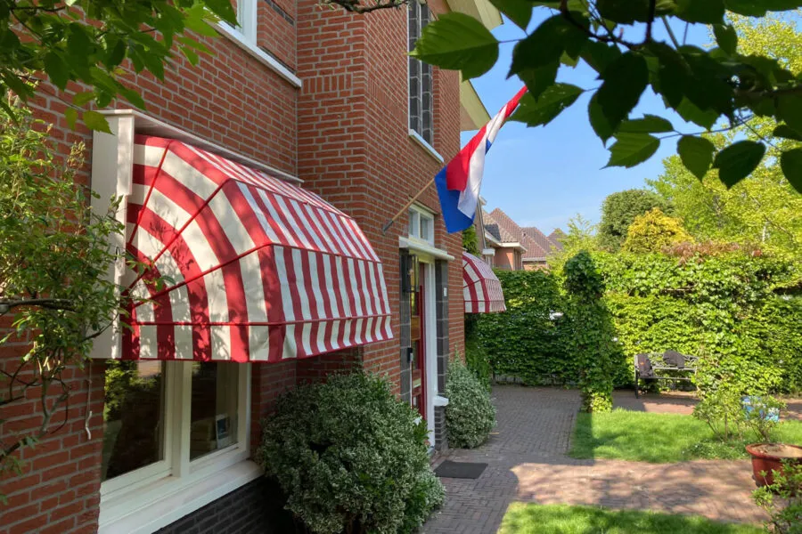 Rood-wit gestreepte markiezen aan de gevel van een jaren-30 woning