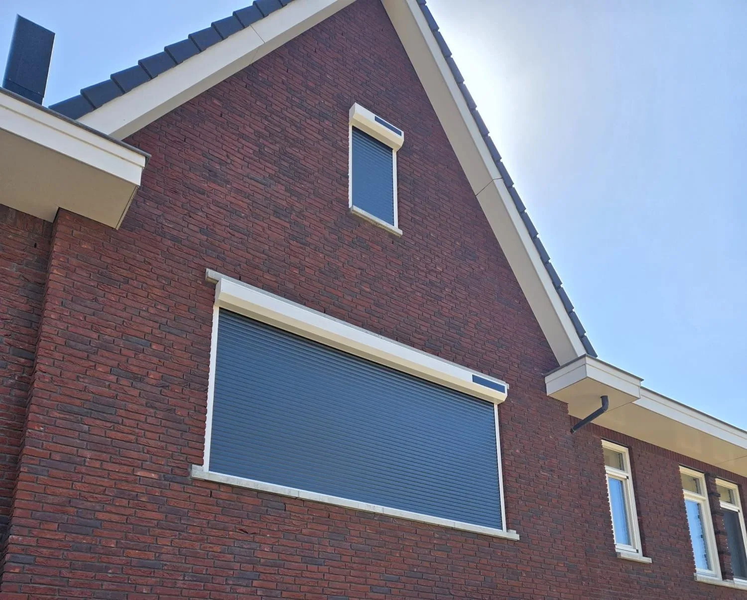 Neergelaten rolluik op de zonnige gevel van een woning met rode bakstenen