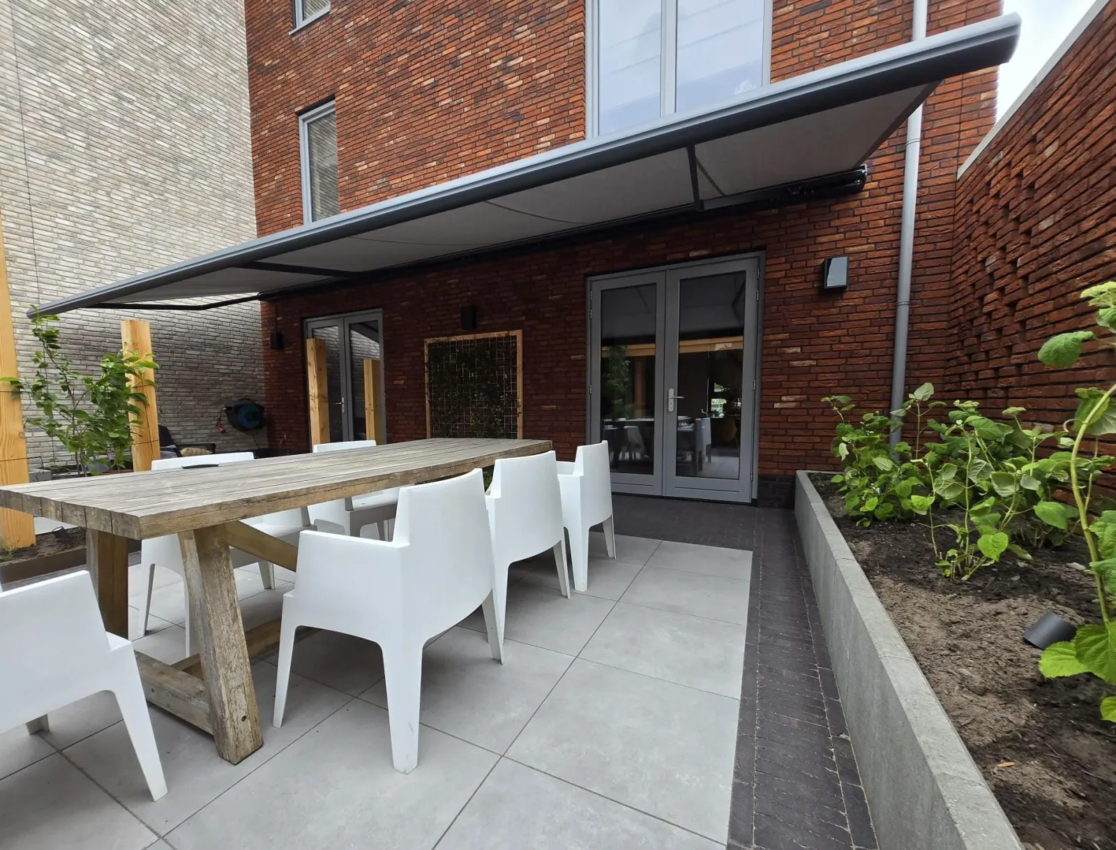 Knikarmscherm met grijs doek boven een terras met eettafel