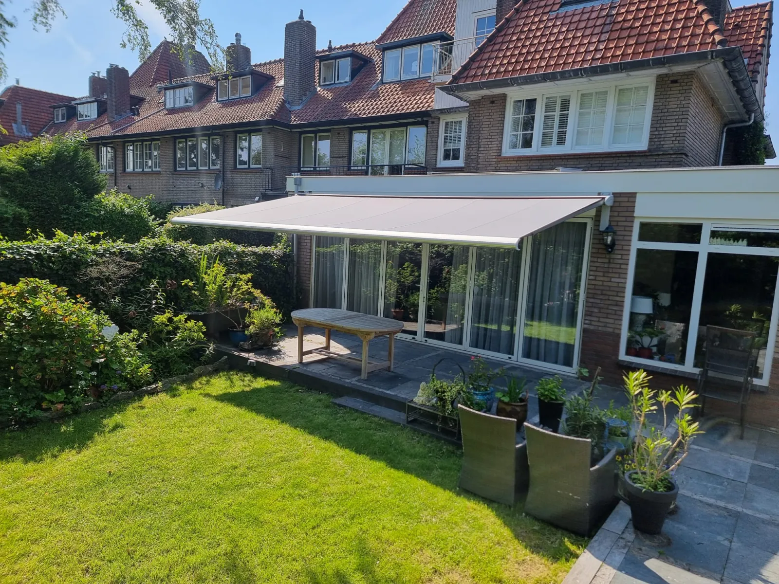 Uitgerold knikarmscherm boven een terras aan de achtergevel van een woning