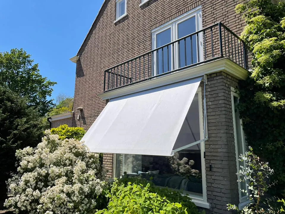 Wit uitvalscherm van IWS Zonwering dat de felle zon opvangt boven een woonkamerraam