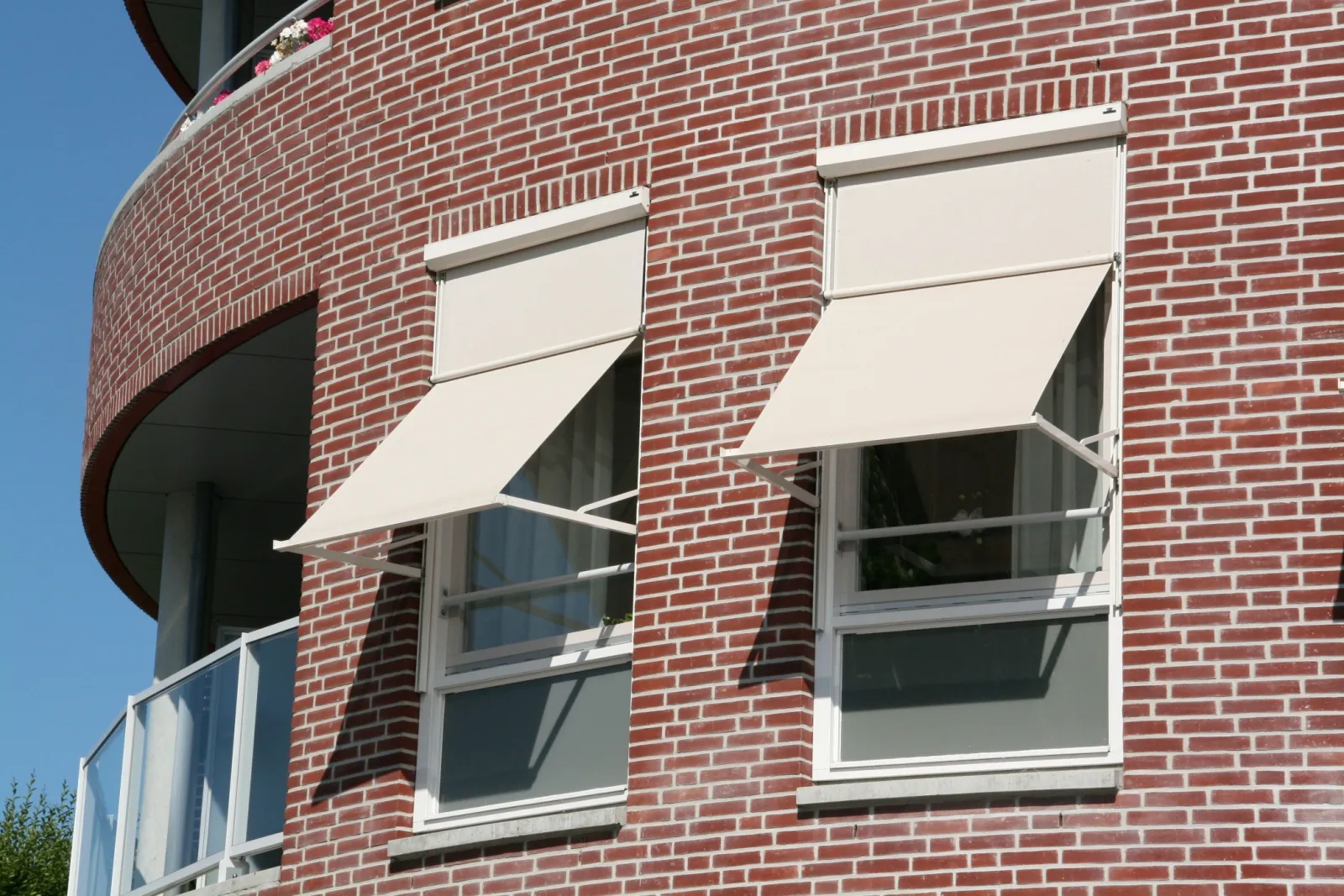 Twee cremekleurige uitvalschermen met een compacte kast boven het kozijn, strak in de gevel