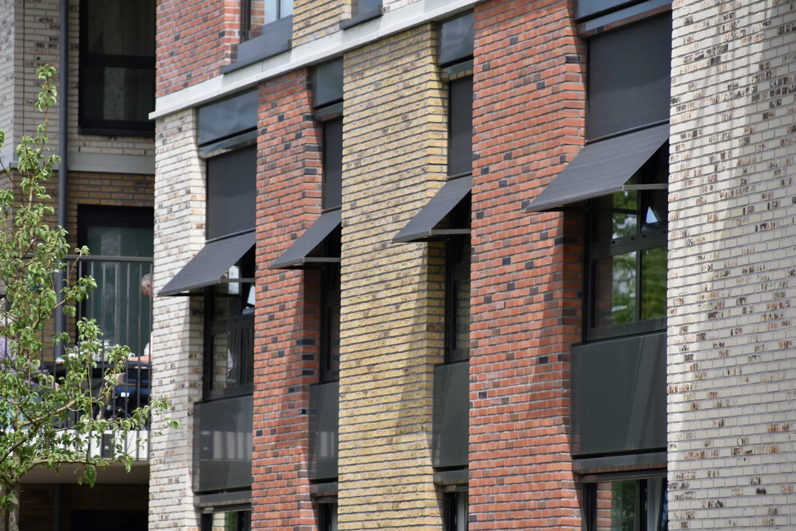 Antracietkleurige uitvalschermen die dicht bij de gevel blijven boven de ramen van een modern gebouw