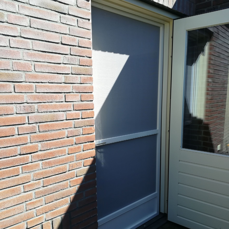 Scharnierende hordeur met kattenluik, gemonteerd tussen twee bakstenen gevelvlakken