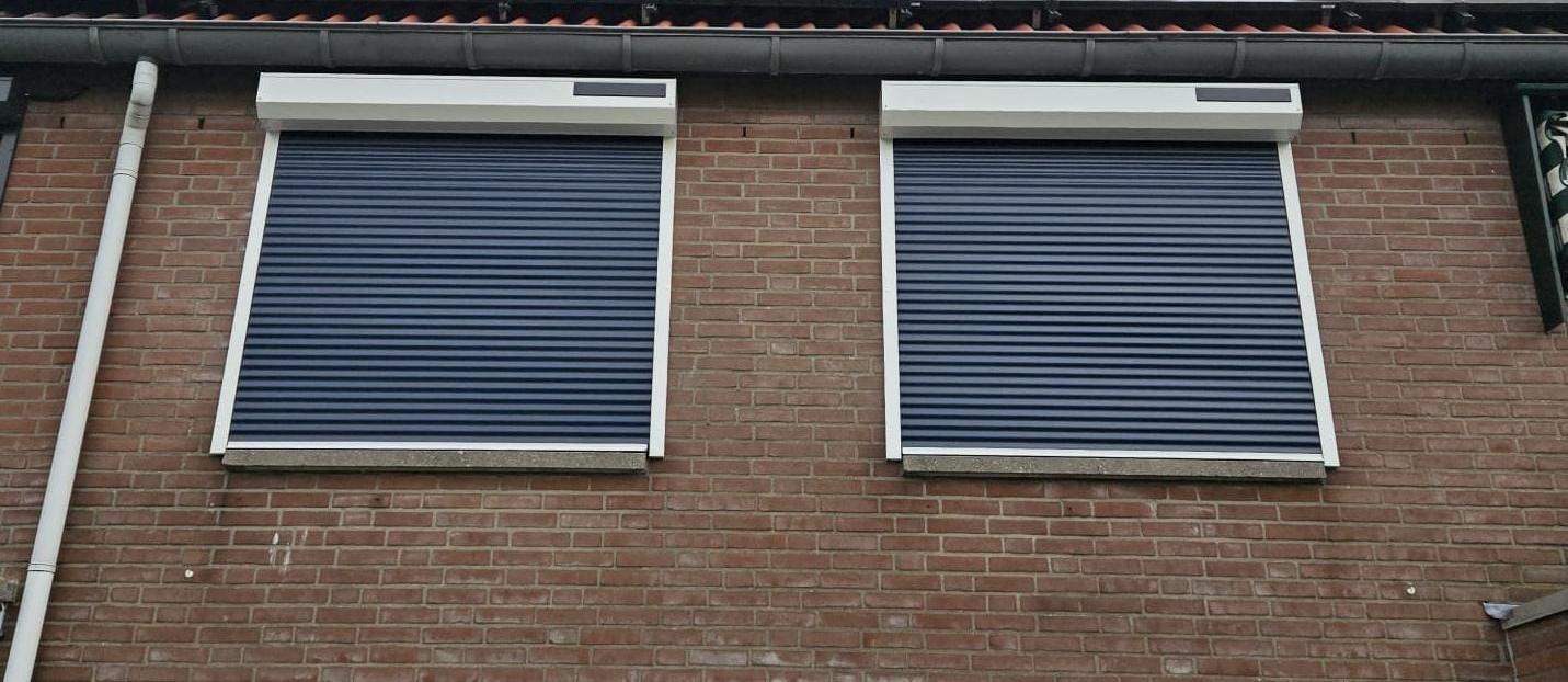 Twee neergelaten solar rolluiken naast elkaar op een bakstenen gevel