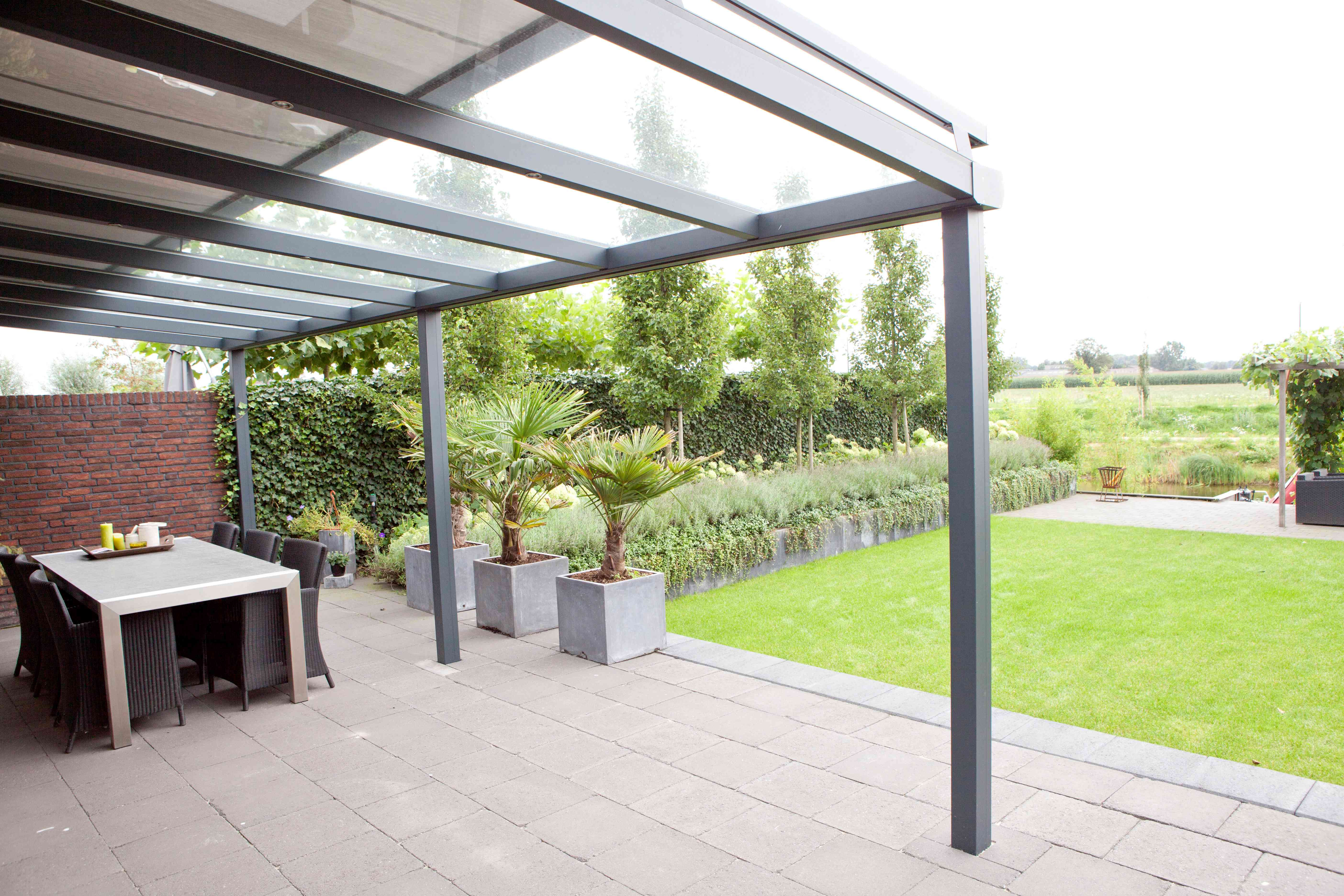 Veranda met glazen dak en zonwering onder het glas, met terras en tuin op de achtergrond